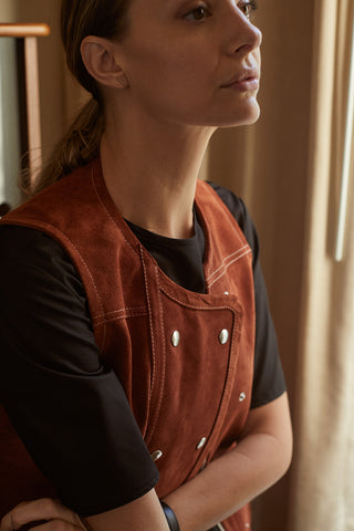 Close up of a woman standing in her office. She is wearing Field Trip's half sleeve in black under a rust-colored suede vest.