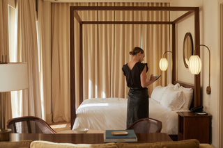 A woman in a hotel room, working on an iPad. She is wearing Field Trip's Reversible Flutter Sleeve in Black paired with a black leather pencil skirt.